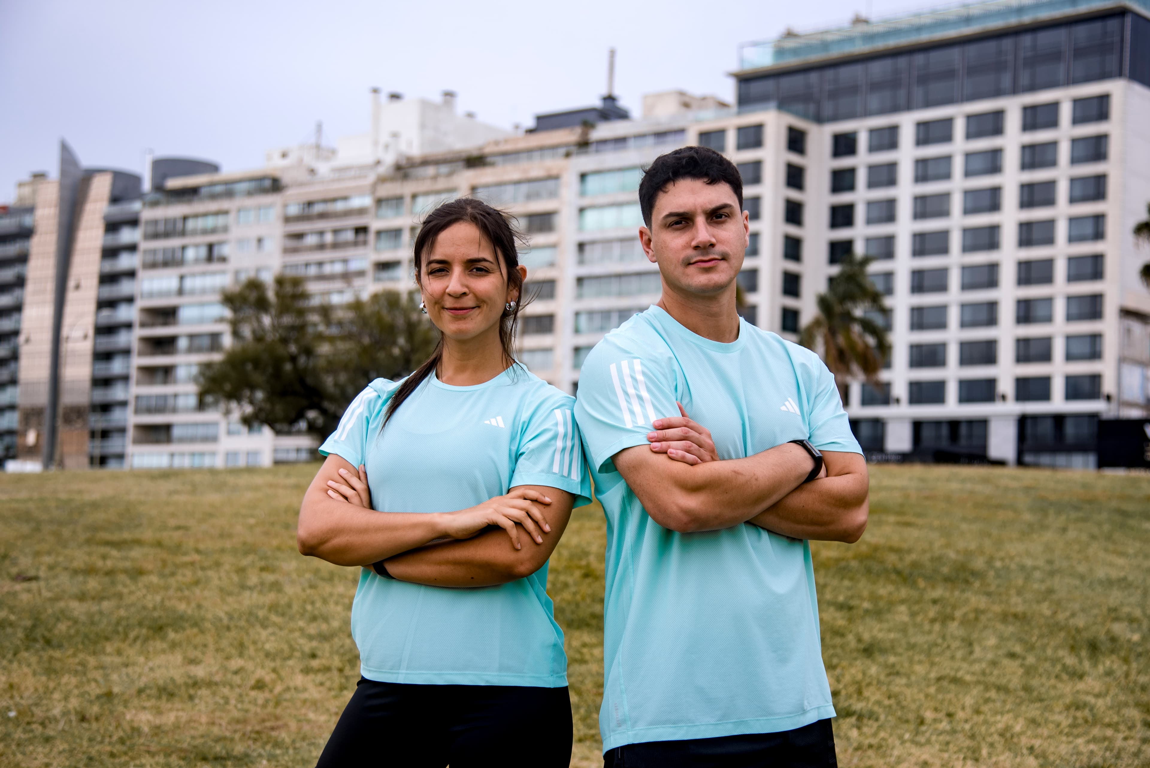 Nico Cardozo y Stephie Galliazzi mirando a la cámara, ambos cruzando los brazos, en un parque